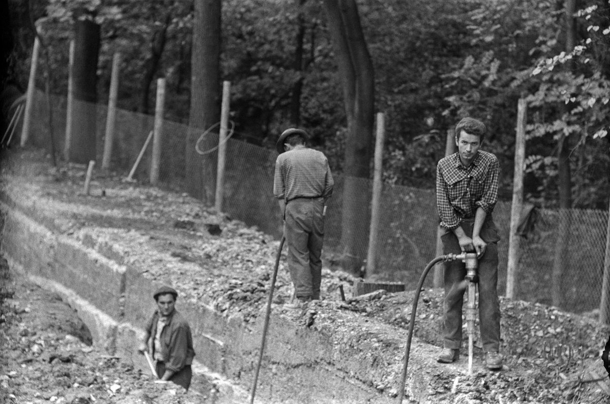 Zu sehen sind drei Männer in und an einer Baugrube bei der Arbeit