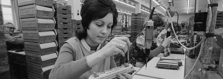 Zu sehen ist eine Frau in einer Produktionshalle, die einen Modellzug hält und an diesem schraubt.